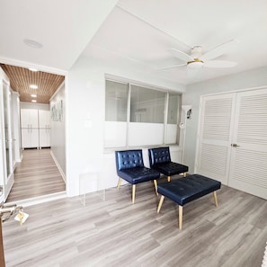 A modern interior with a ceiling fan, a large window, and a seating area with two chairs and a bench. - Enjoy beautiful oceanfront views of the Ocean City coastline in this one bedroom, one bath condo located just a few steps from the beach! (Ocean City)