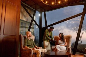 A room with a large window, a wooden ceiling, and a circular light fixture. - Newburgh Ella - The Tea Factory Resort (Ella)