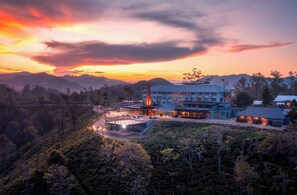 A hotel with a large building, outdoor seating area, and a view of the surrounding hills. - Newburgh Ella - The Tea Factory Resort (Ella)