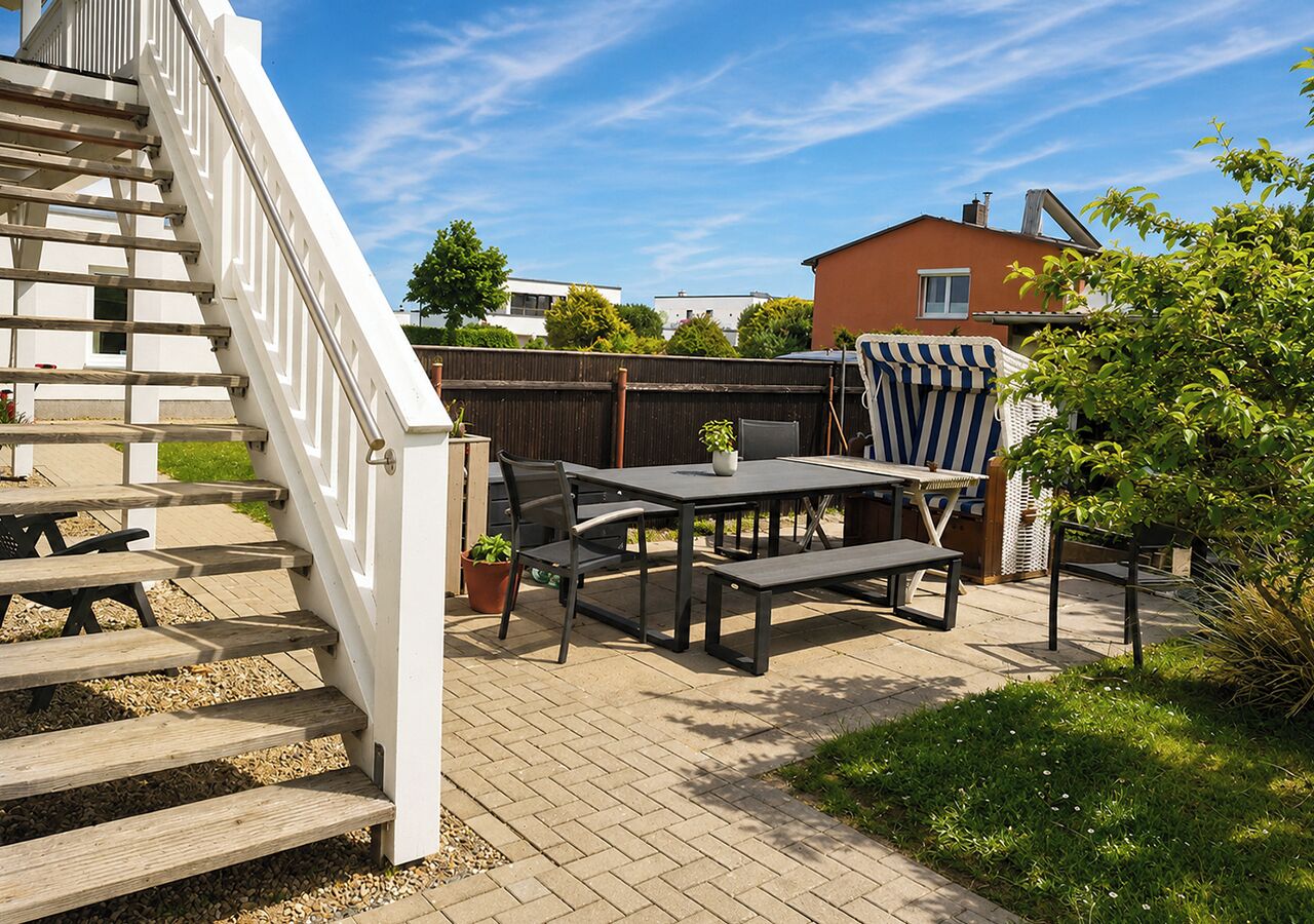 Eine Terrasse mit einer Holztreppe, einem Tisch mit Stühlen und einem Streifenstuhl.