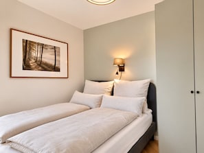 A bedroom with a bed, two pillows, a wall-mounted lamp, and a framed picture.