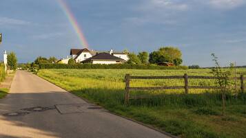 Eine ländliche Straße mit Regenbogen, einem weißen Haus und einem Holzzaun.