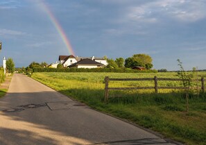 Een landweg met een regenboog, een wit huis en een houten hek.