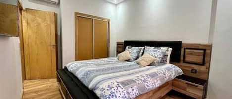 A bedroom with a bed, wooden wardrobe, bedside table, and a bench.