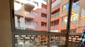 A balcony with a white table and chairs, a view of adjacent buildings, and a window with a decorative grille. - Bel Appartement en Résidence et Piscine (Marrakech)