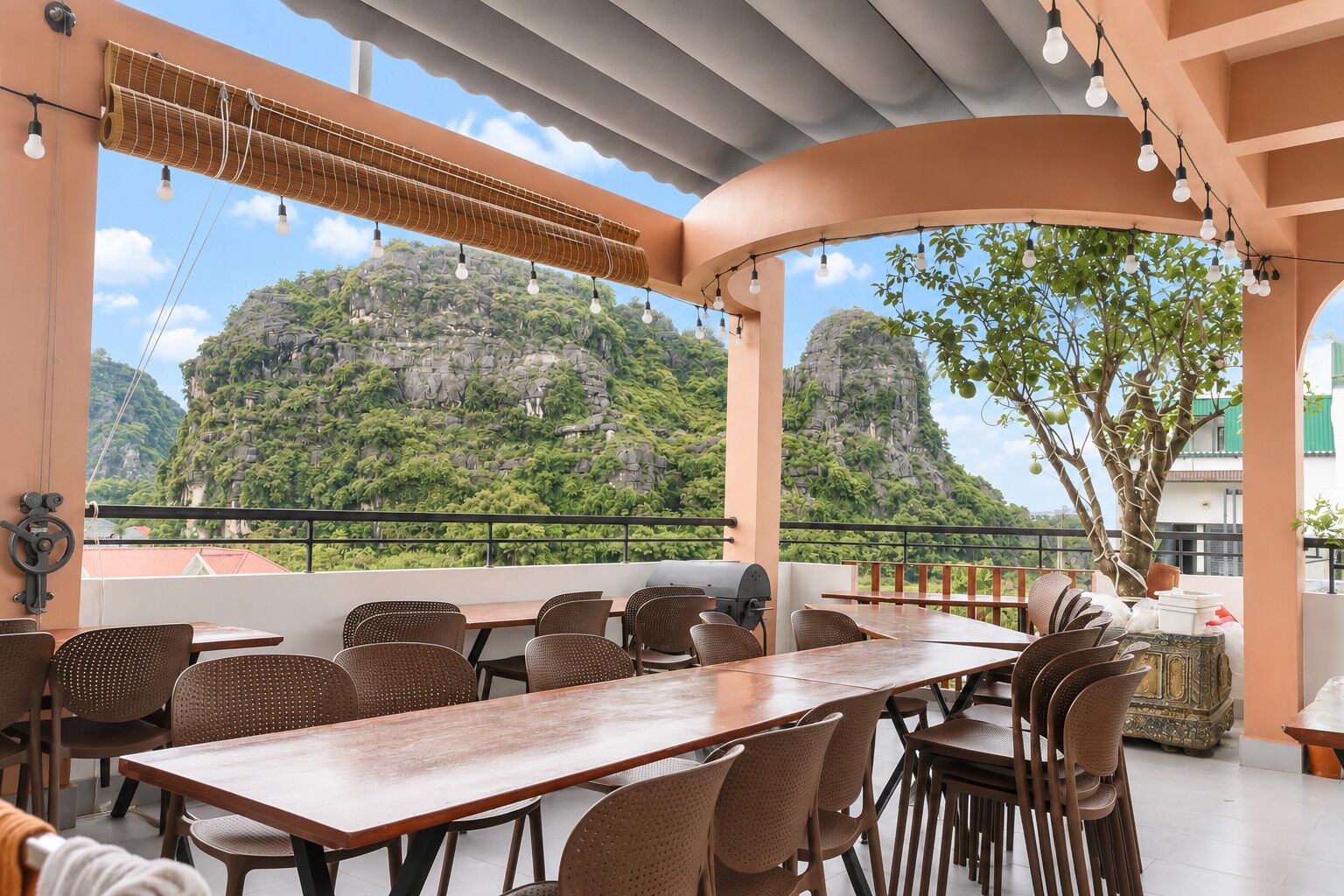 An outdoor dining area with a view of a mountainous landscape, featuring a long table and wicker chairs.