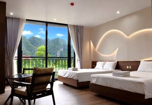 A hotel room with two beds, a chair, and a view of a mountainous landscape through large windows. - Hidden Green Hotel Tam Coc - Ninh Binh (Nam Hoa Lu)