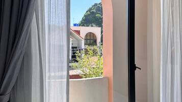 A bedroom with a large window, a bed, and a view of a building and greenery outside.