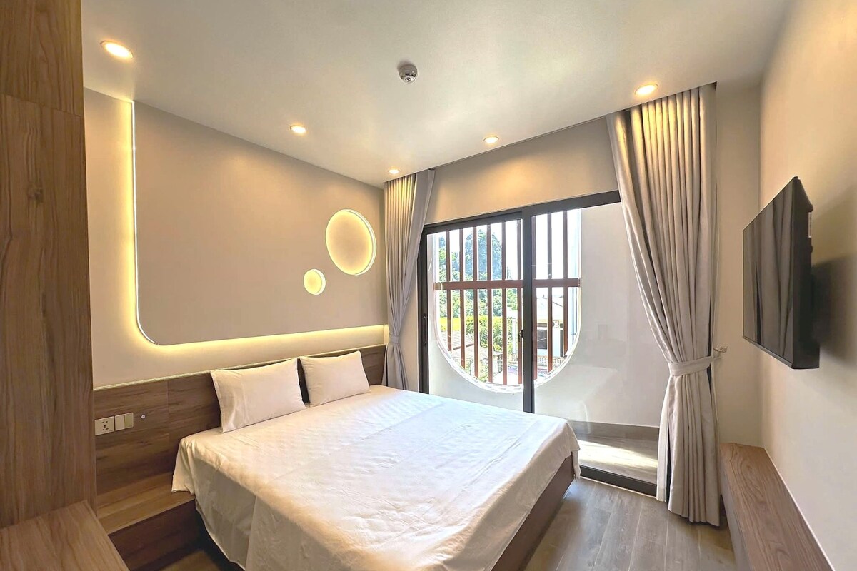 A modern hotel room with a large bed, a TV, and a window with curtains.