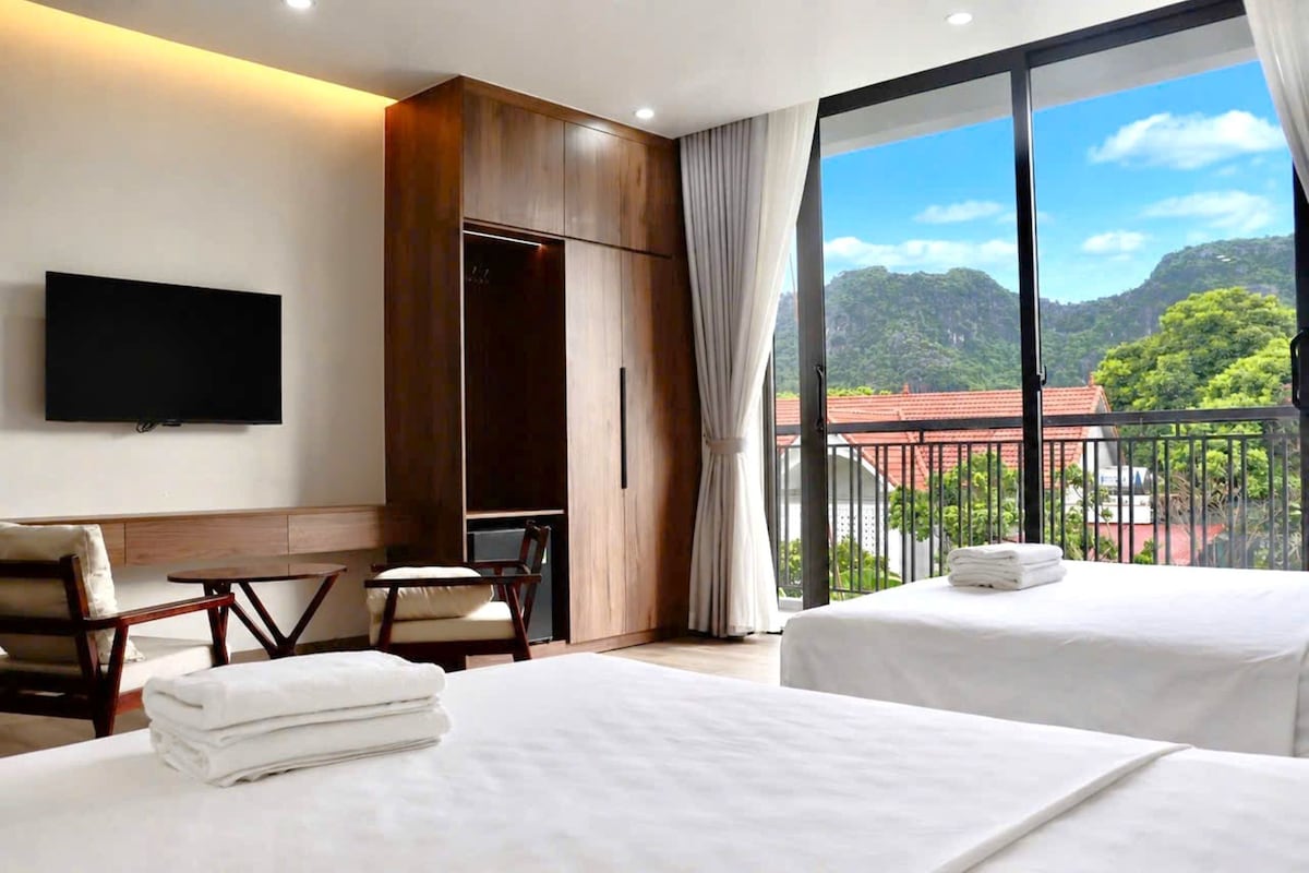 A hotel room with two beds, a TV, a wardrobe, and a balcony with a mountain view.