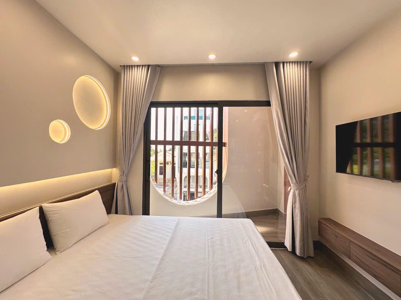A modern hotel room with a large bed, a TV mounted on the wall, and a balcony with curtains.