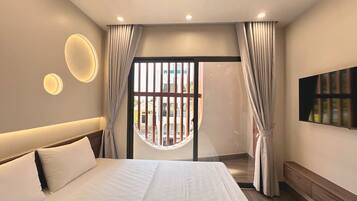 A modern hotel room with a large bed, a TV mounted on the wall, and a balcony with curtains.