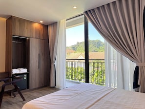 A hotel room with a bed, a desk, a wardrobe, and a balcony with a view of greenery. - Hidden Green Hotel Tam Coc - Ninh Binh (Nam Hoa Lu)