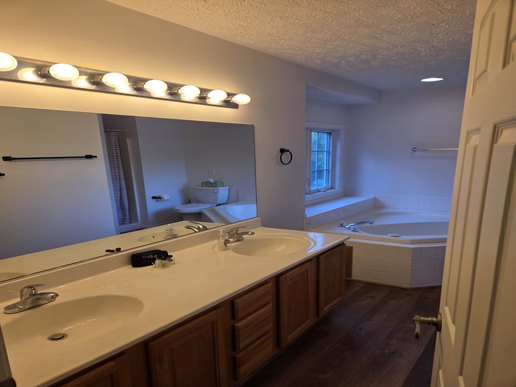 A bathroom with a double sink vanity, a large mirror, and a bathtub.