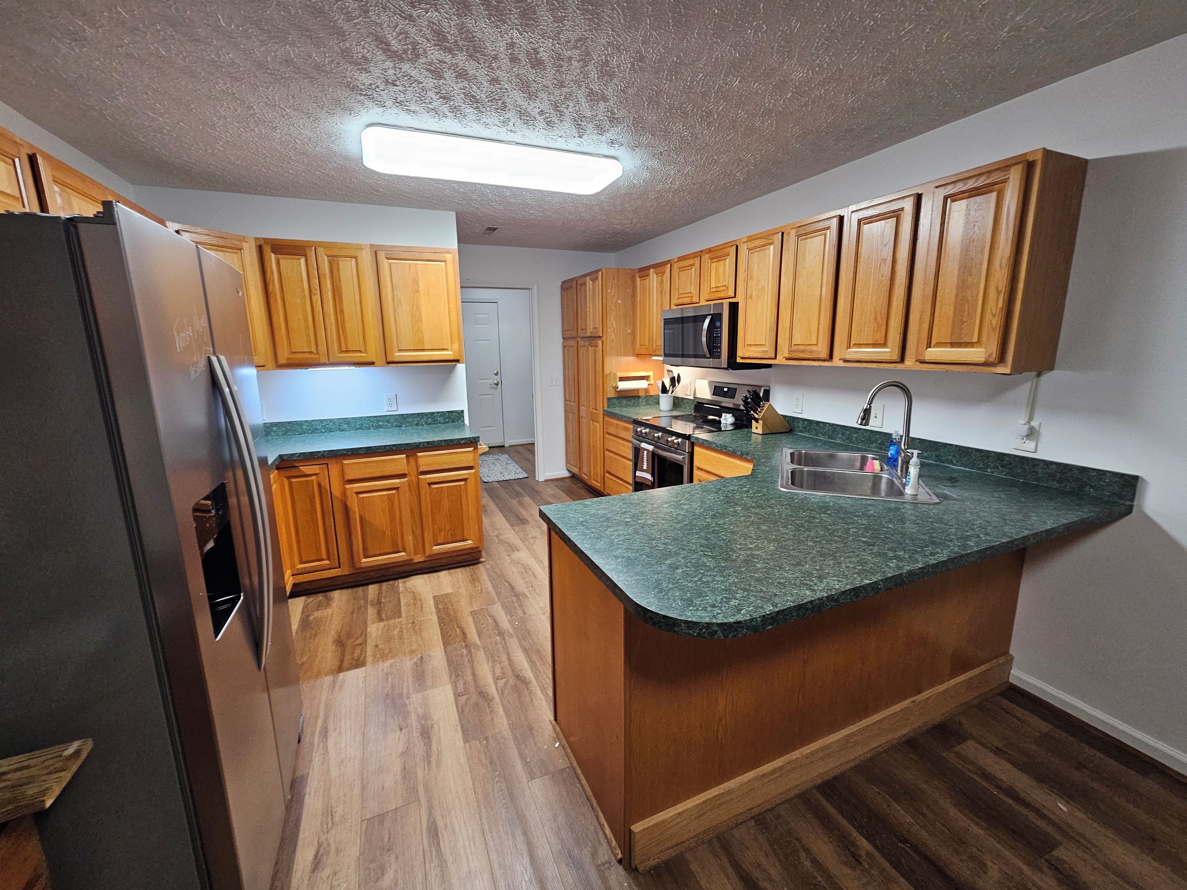 A kitchen with wooden cabinets, a stainless steel sink, a microwave, and a refrigerator.