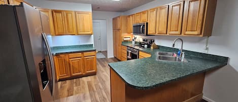Una cocina con gabinetes de madera, un lavamanos de acero inoxidable, un microondas y un refrigerador.