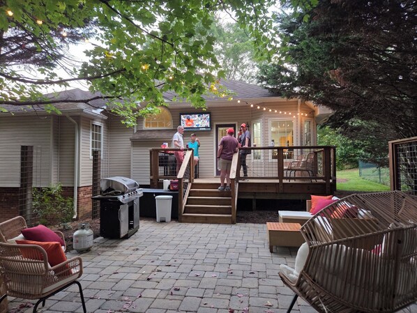 A backyard patio with a grill, outdoor seating, and a TV screen.