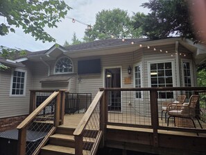 A house with a wooden deck, a staircase, and a porch area with chairs.