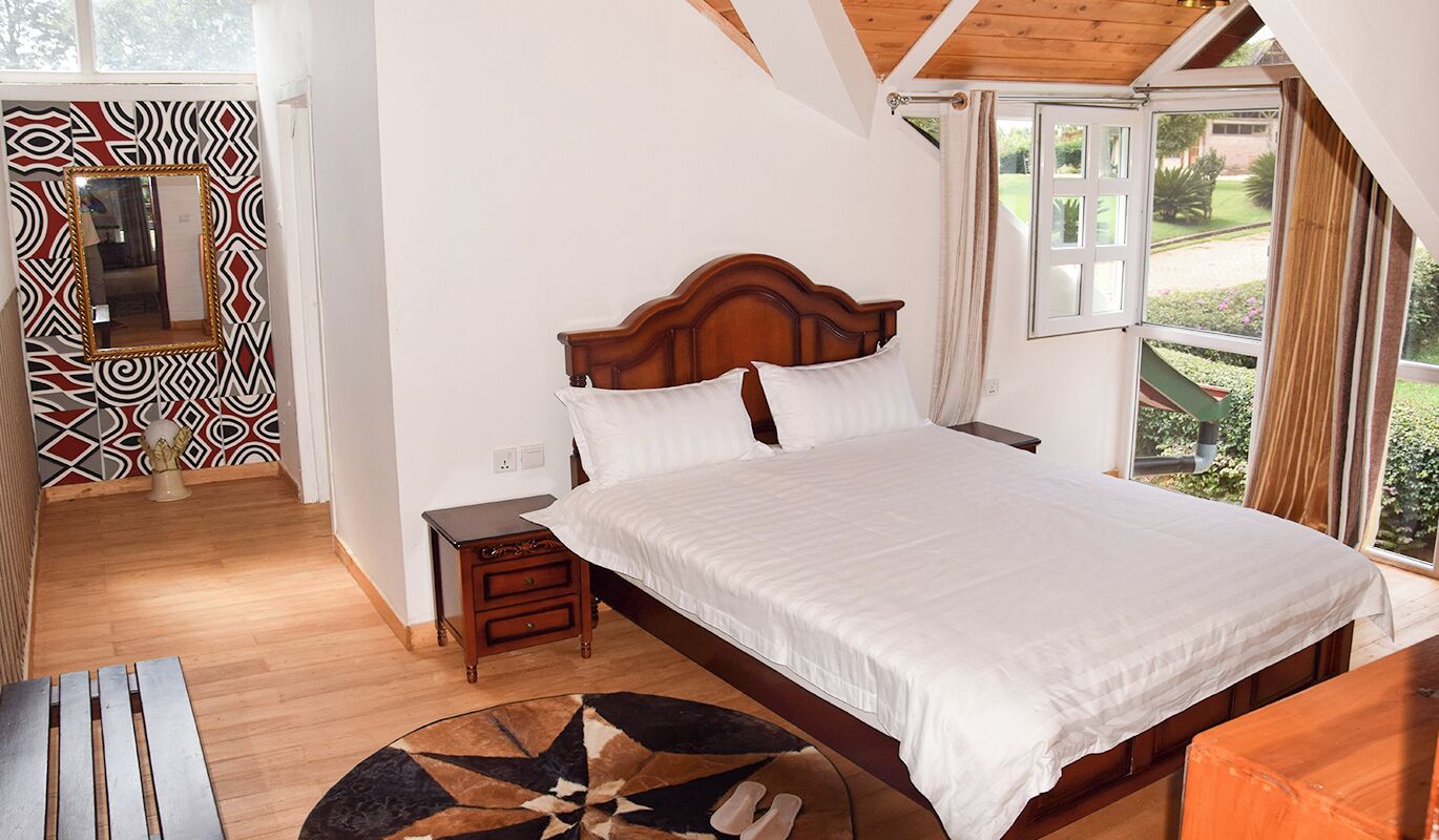 Un dormitorio con cama de madera, una mesita de noche, una mesa redonda y una ventana con vistas a zonas verdes.