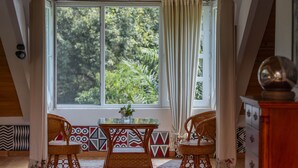 Una habitación acogedora con un ventanal grande, dos sillones de mimbre, una mesita y un jarrón decorativo.