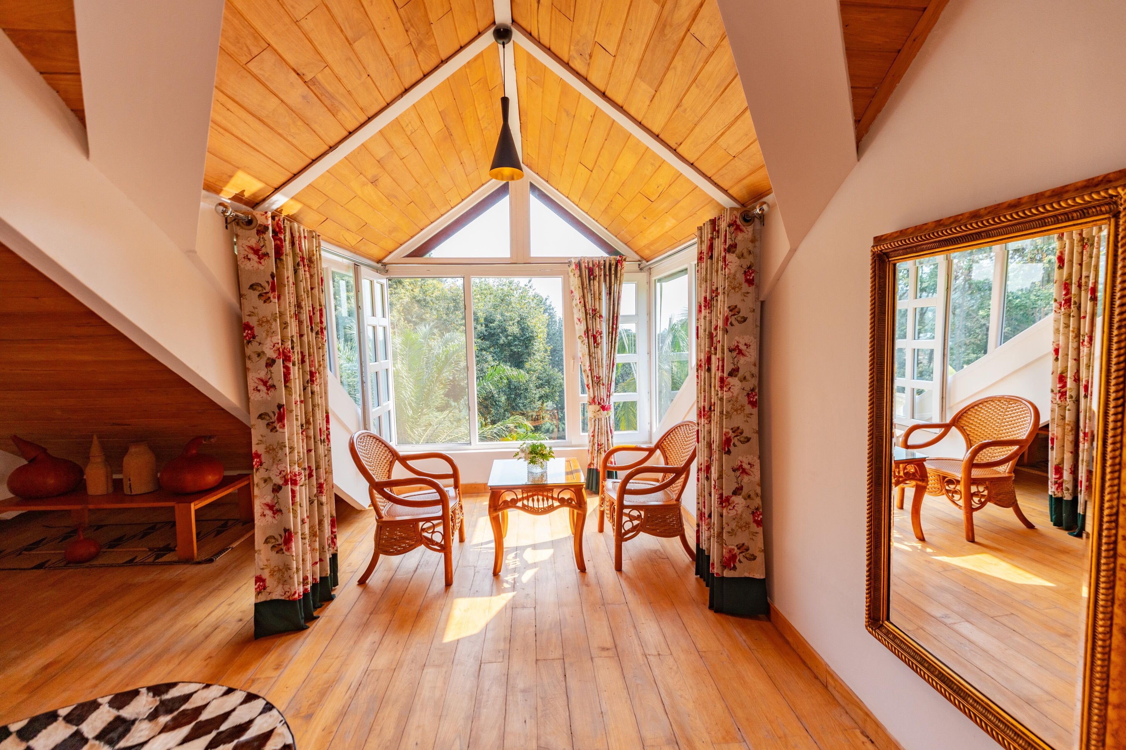 Habitación con techo alto, vigas de madera, un espejo grande y dos sillas de mimbre alrededor de una pequeña mesa.