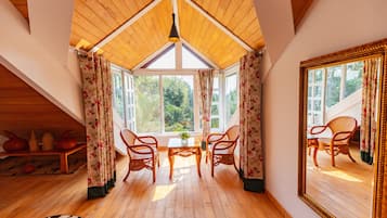 Habitación con techo alto, vigas de madera, un espejo grande y dos sillas de mimbre alrededor de una pequeña mesa.