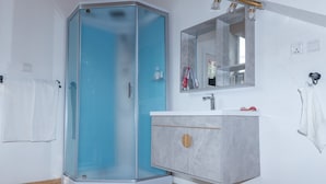 Un baño moderno con cabina de ducha de vidrio, tocador de mármol y un espejo grande sobre el lavabo.
