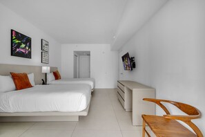 A modern hotel room with two beds, a desk, a chair, and artwork on the walls. - Oceanview Highrise - Amenities (Hollywood)