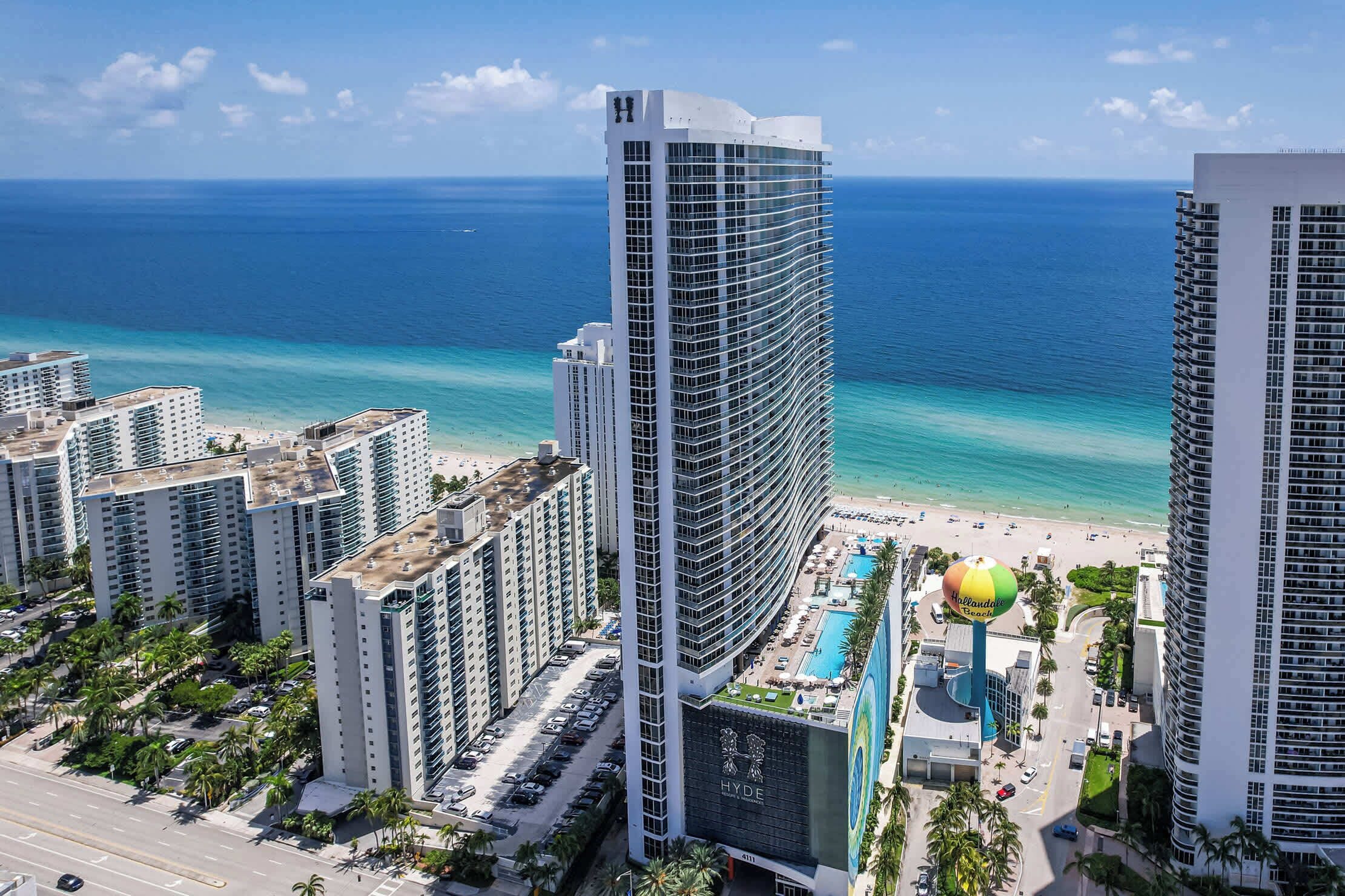 Ein Hochhotel mit Pool und Blick auf den Strand, umgeben von anderen Gebäuden und Palmen.
