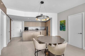 A modern kitchen with a central island, a dining area with a round table and chairs, and a painting on the wall. - Oceanview Highrise - Amenities (Hollywood)