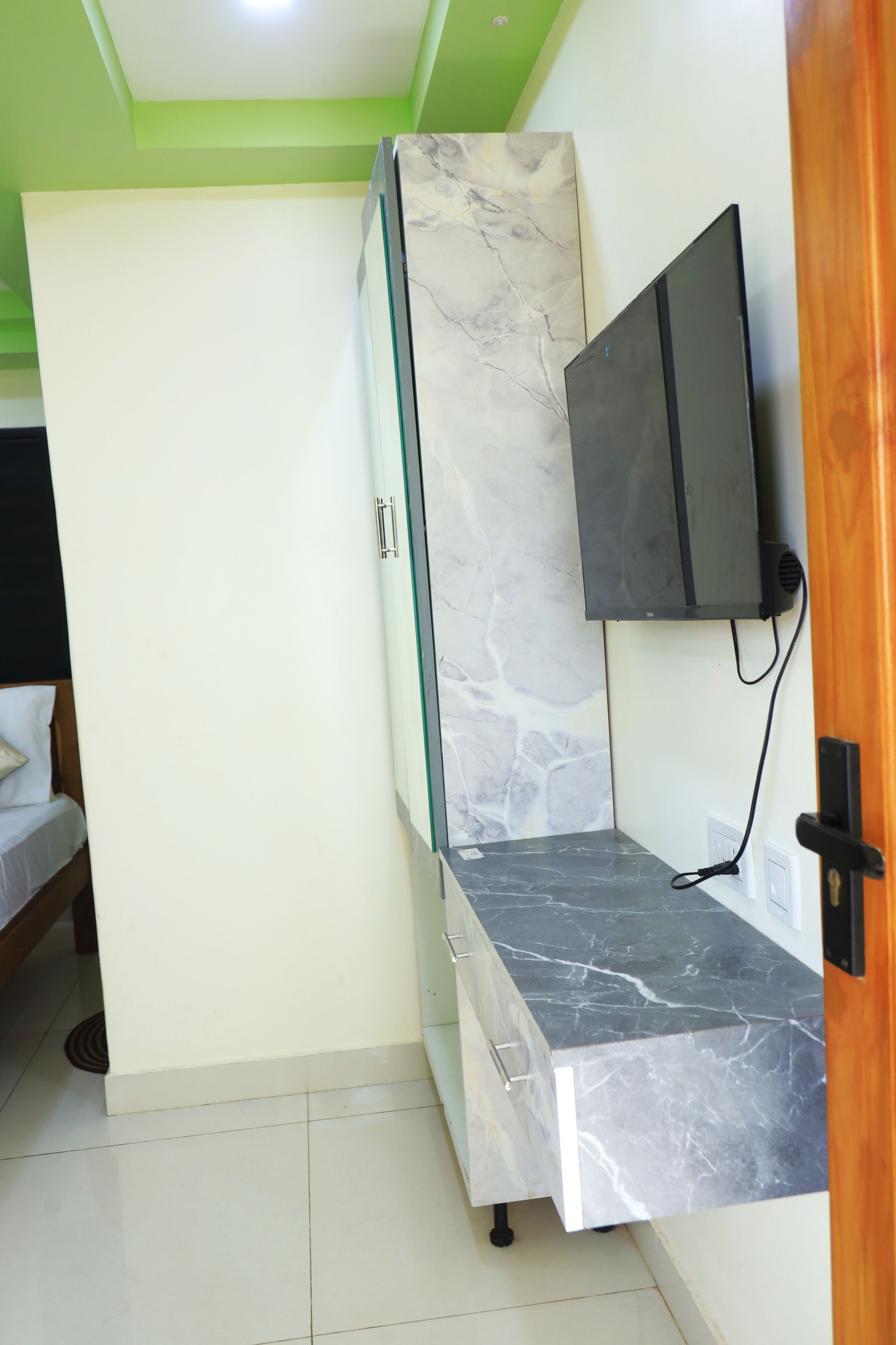 A room with a bed, a TV mounted on the wall, and a marble-patterned cabinet.
