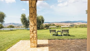 A stone pillar, two covered chairs, and a view of a grassy field with distant hills.