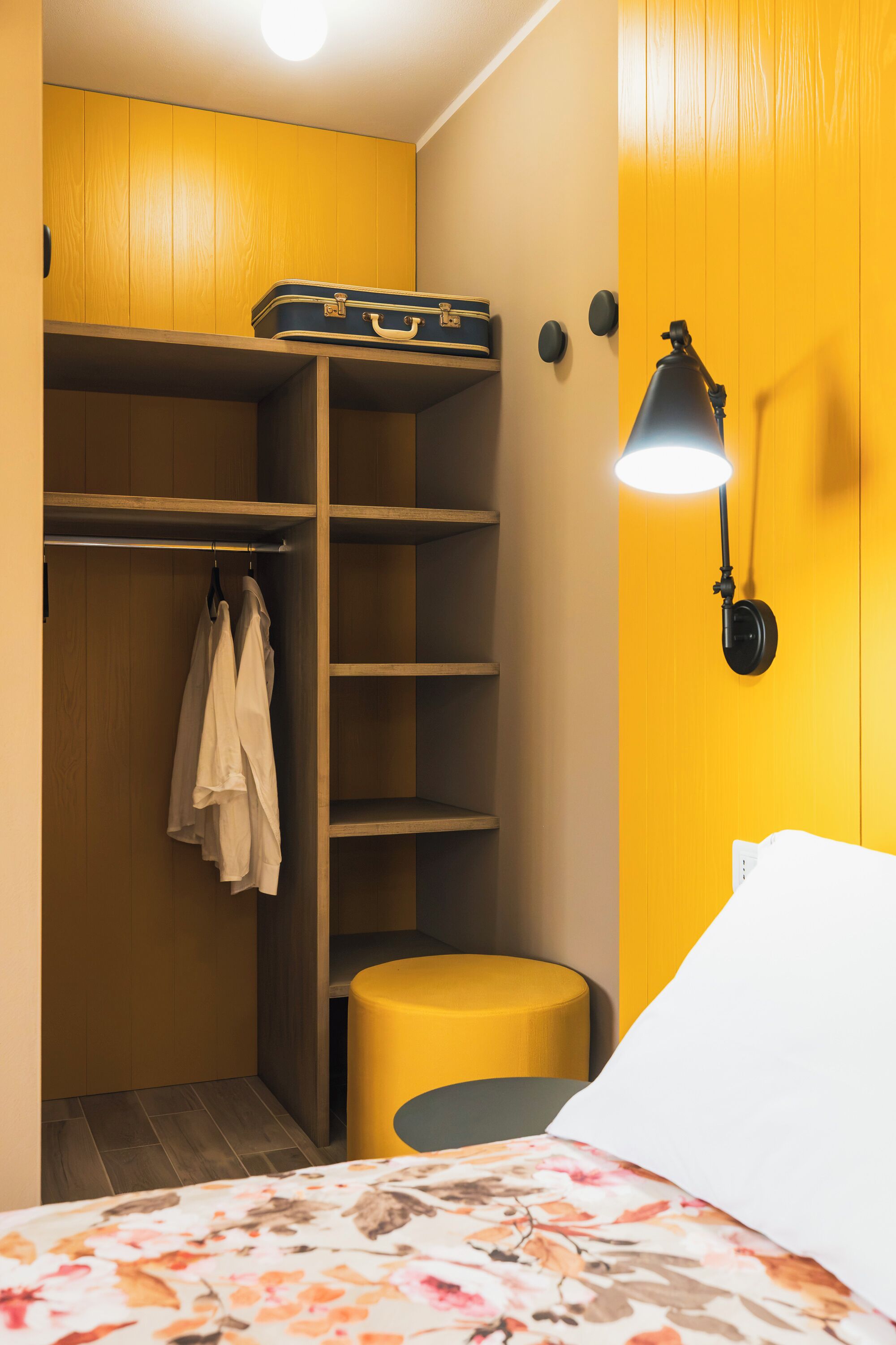 Ein kleines Zimmer mit Bett, Sitzbank, Kleiderschrank und Wandlampe.