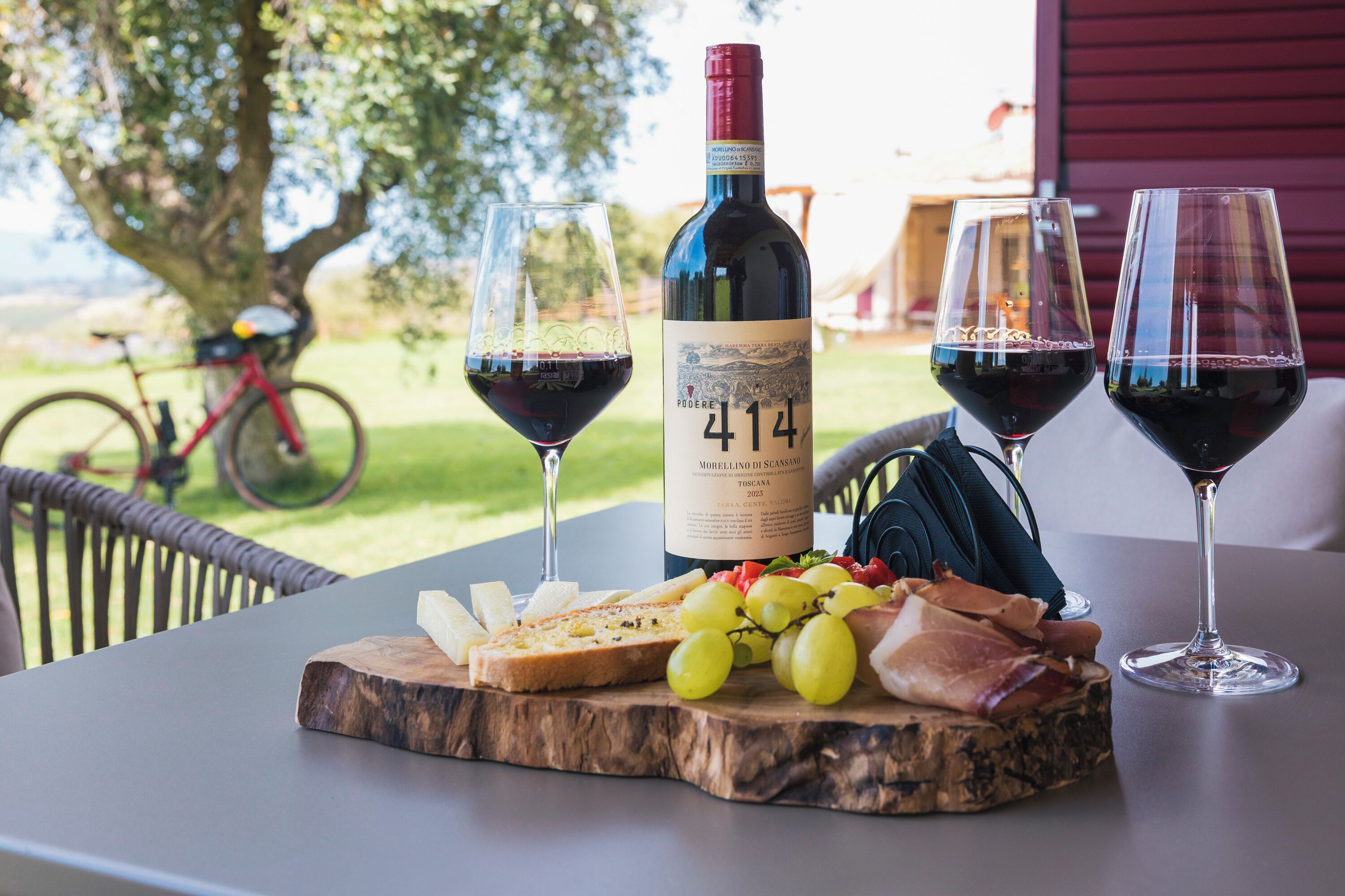 A table with a bottle of wine, glasses, and a wooden board with cheese and grapes.