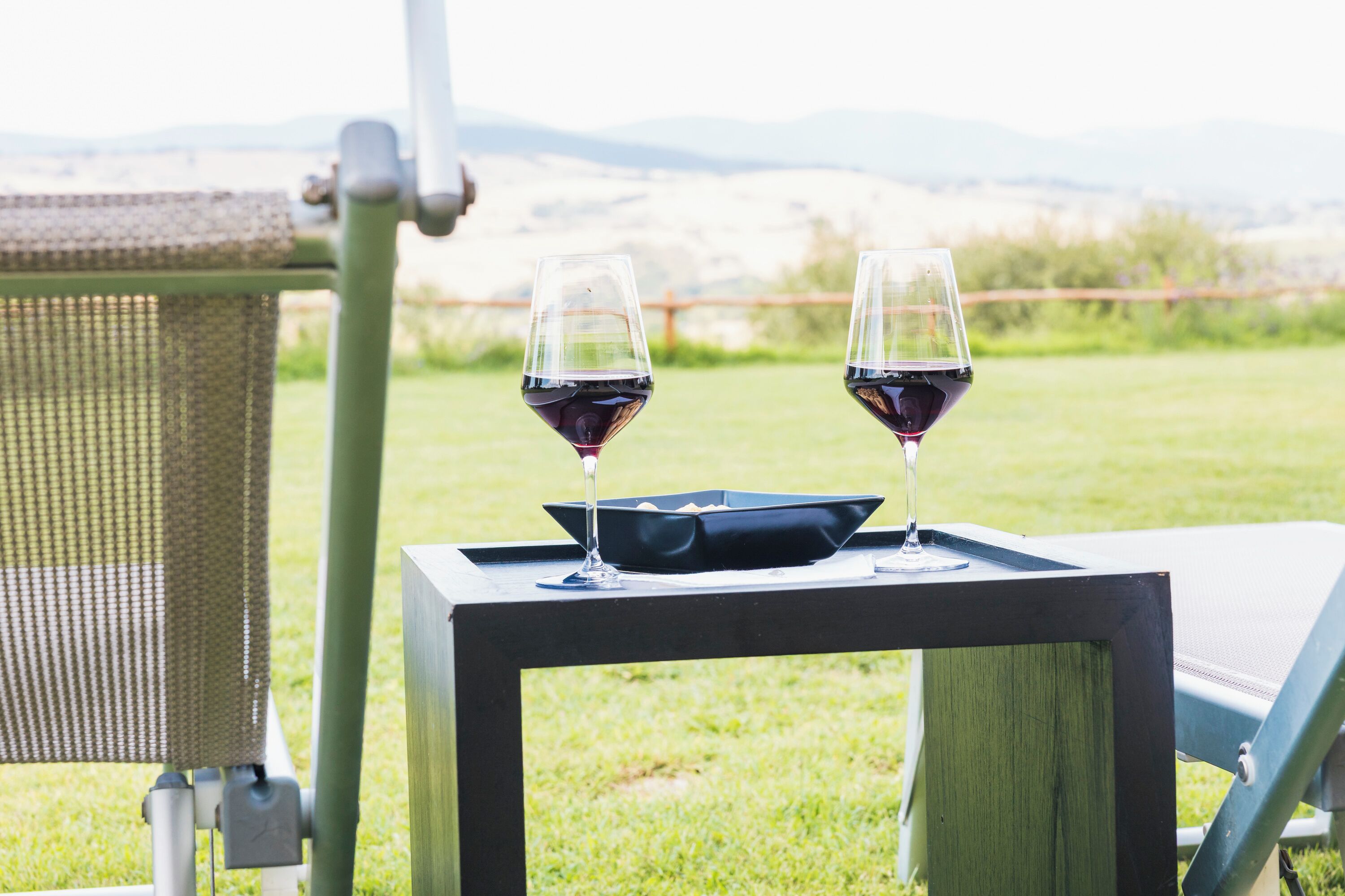 Zwei Gläser Rotwein auf einem quadratischen Tisch mit Blick auf die Landschaft.