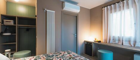 Un dormitorio moderno con cama, armario, radiador, ventana con cortinas y escritorio con lámpara.