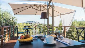Un espace de restauration en plein air, avec des tables, des chaises, des parasols et une vue sur une colline.