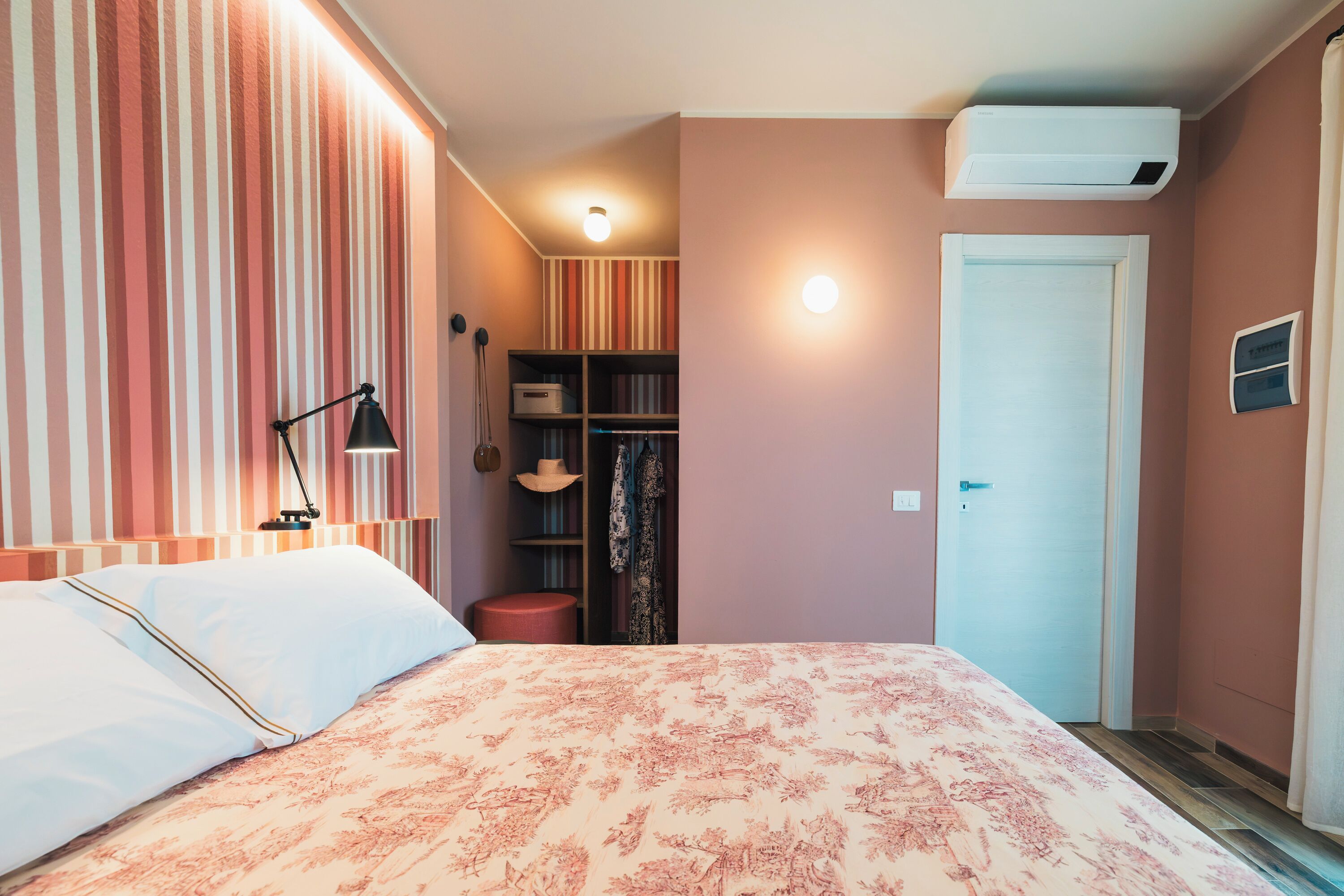 A bedroom with a bed, a nightstand, a lamp, a wardrobe, and a door.
