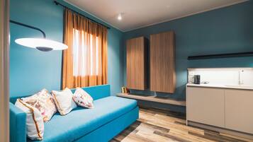 Ein modernes Zimmer mit einem blauen Sofa, Holzschränken, einer Küchenzeile und einem Fenster mit Vorhängen.