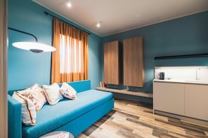 Ein modernes Zimmer mit einem blauen Sofa, Holzschränken, einer Küchenzeile und einem Fenster mit Vorhängen.