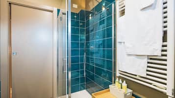 A modern bathroom with a glass shower enclosure, a wooden vanity with toiletries, and a towel rack.