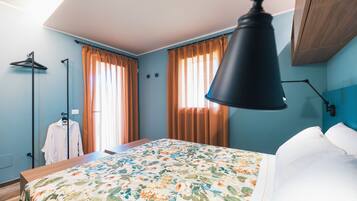 Quarto de hotel com cama, luminária pendente, guarda-roupa e janela com cortinas.