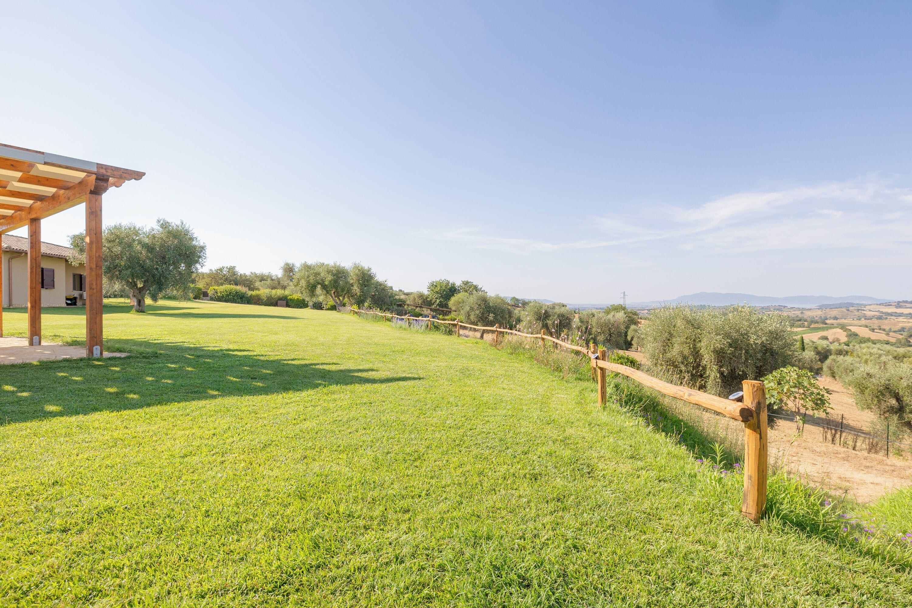 A grassy outdoor area with a wooden pergola and a view of the countryside.