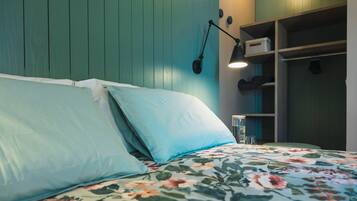 Ein Bett mit floraler Bettwäsche, eine türkisene Wand und ein Regal mit Gegenständen.