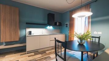 Eine moderne Küche mit integriertem Mikrowellenherd, Spüle und Herd. Ein Esstisch mit Stühlen und eine Vase mit Blumen sind ebenfalls vorhanden. Der Raum hat Holzböden und blaue Wände.