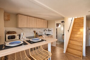 A modern kitchen with a dining area, wooden cabinets, a microwave, and a glass door leading to a bathroom. - Le Pavot Perché Terrace - Air-Conditioned - Wi-Fi - Downtown (Avignon)