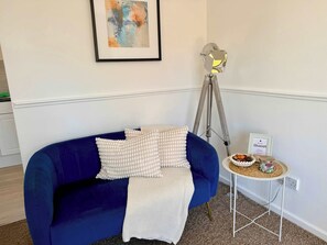 A room with a blue sofa, a white knitted throw, a tripod lamp, and a small table with a sign. - Quiet Shenley Church End | Parking & Balcony (Milton Keynes)
