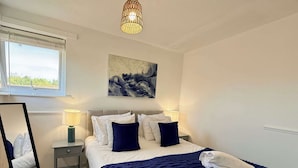 Een slaapkamer met een bed, bedlampen, een spiegel, een schilderij en een raam.