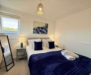 A bedroom with a bed, bedside lamps, a mirror, a painting, and a window. - 2-Bed Milton Keynes Maisonette Parking (Milton Keynes)