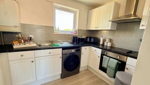 Een functionele keuken met witte kasten, een ingebouwde wasmachine, een magnetron en een kookplaat.